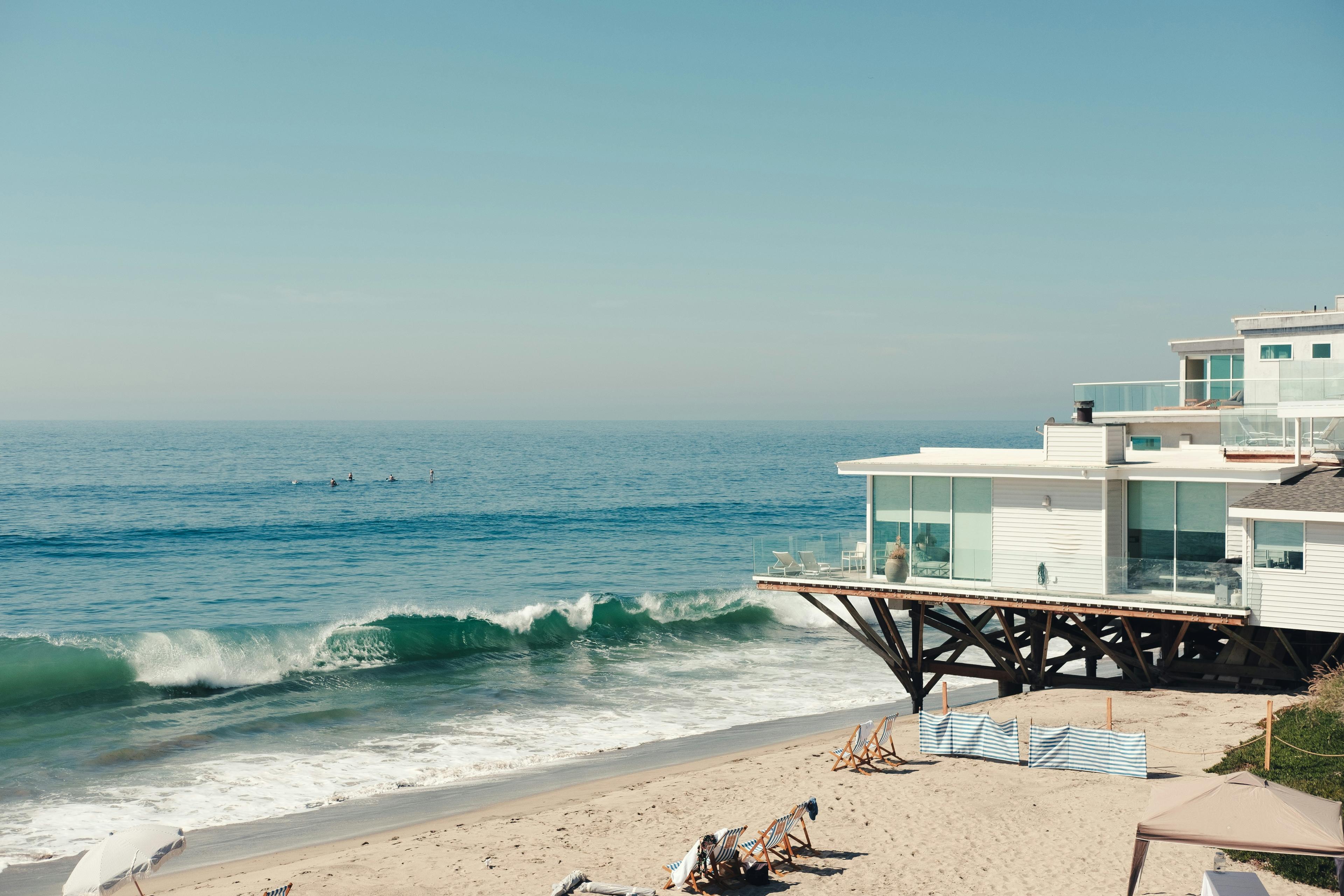 Modern white beach house on stilts with large glass windows by the surf